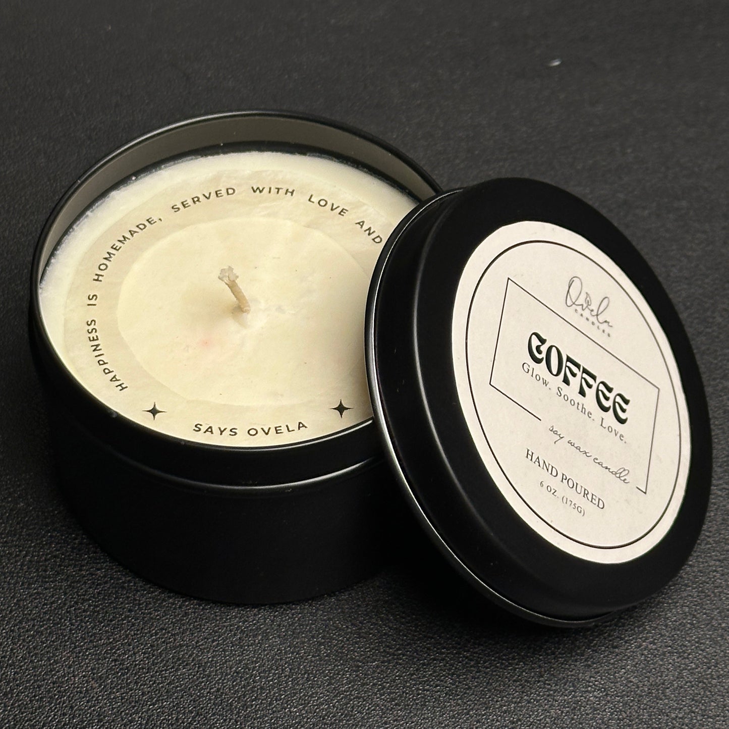 Candle in a black tin with a label on a dark surface
